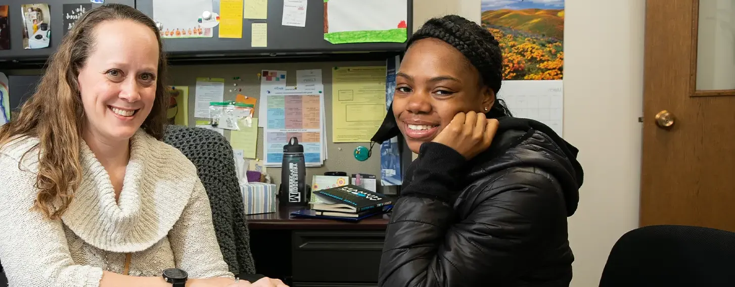 Two women sitting at a desk, looking over a folder together at Student Support.